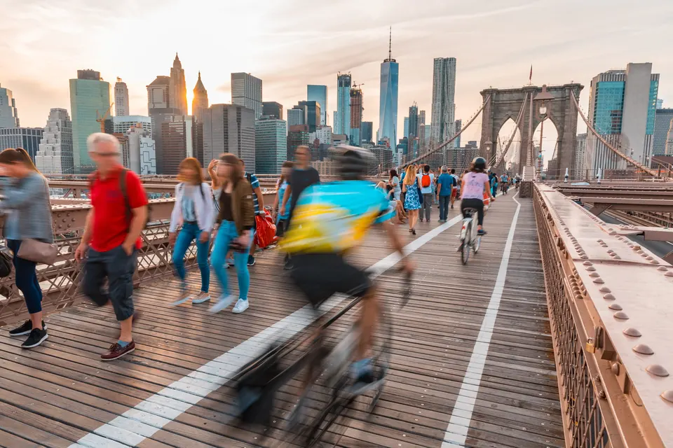 Cyclists crossing the Brooklyn Bridge toward the Manhattan skyline at sunset